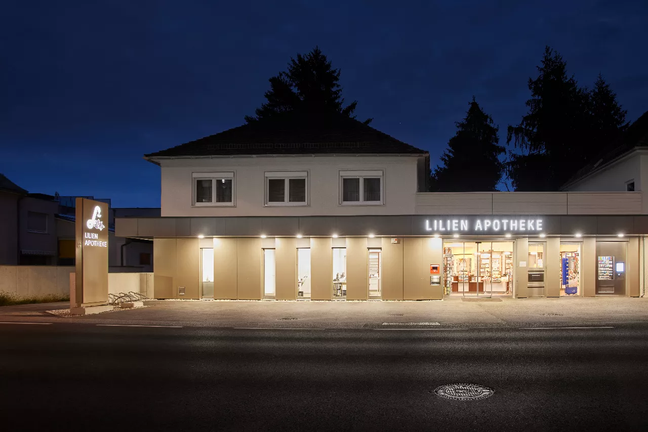 Eine nachts beleuchtete Ladenfront der Lilienapotheke mit eingeschalteten Lichtern