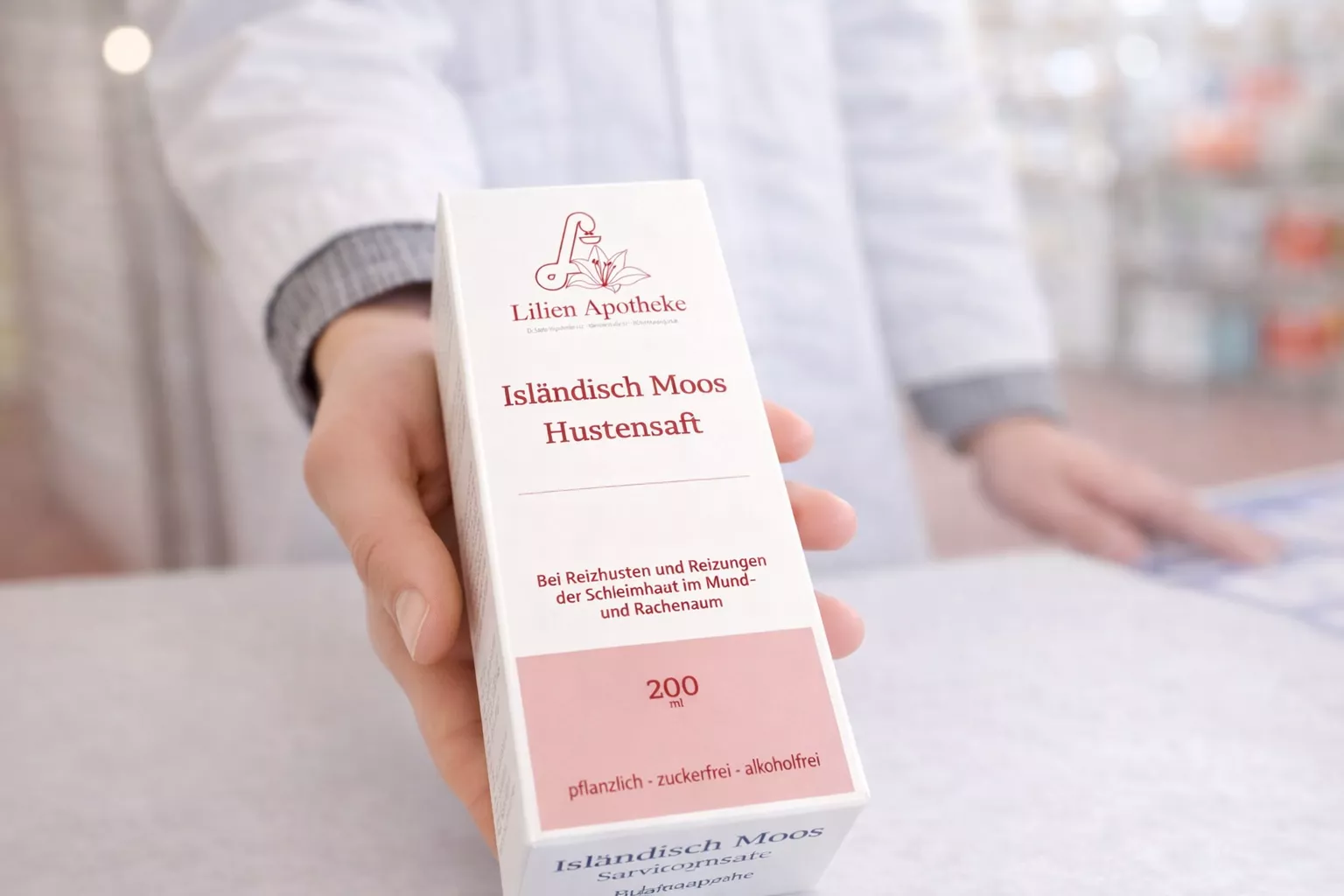 Eine Person hält eine Schachtel mit Hustensaft auf einem Tisch.